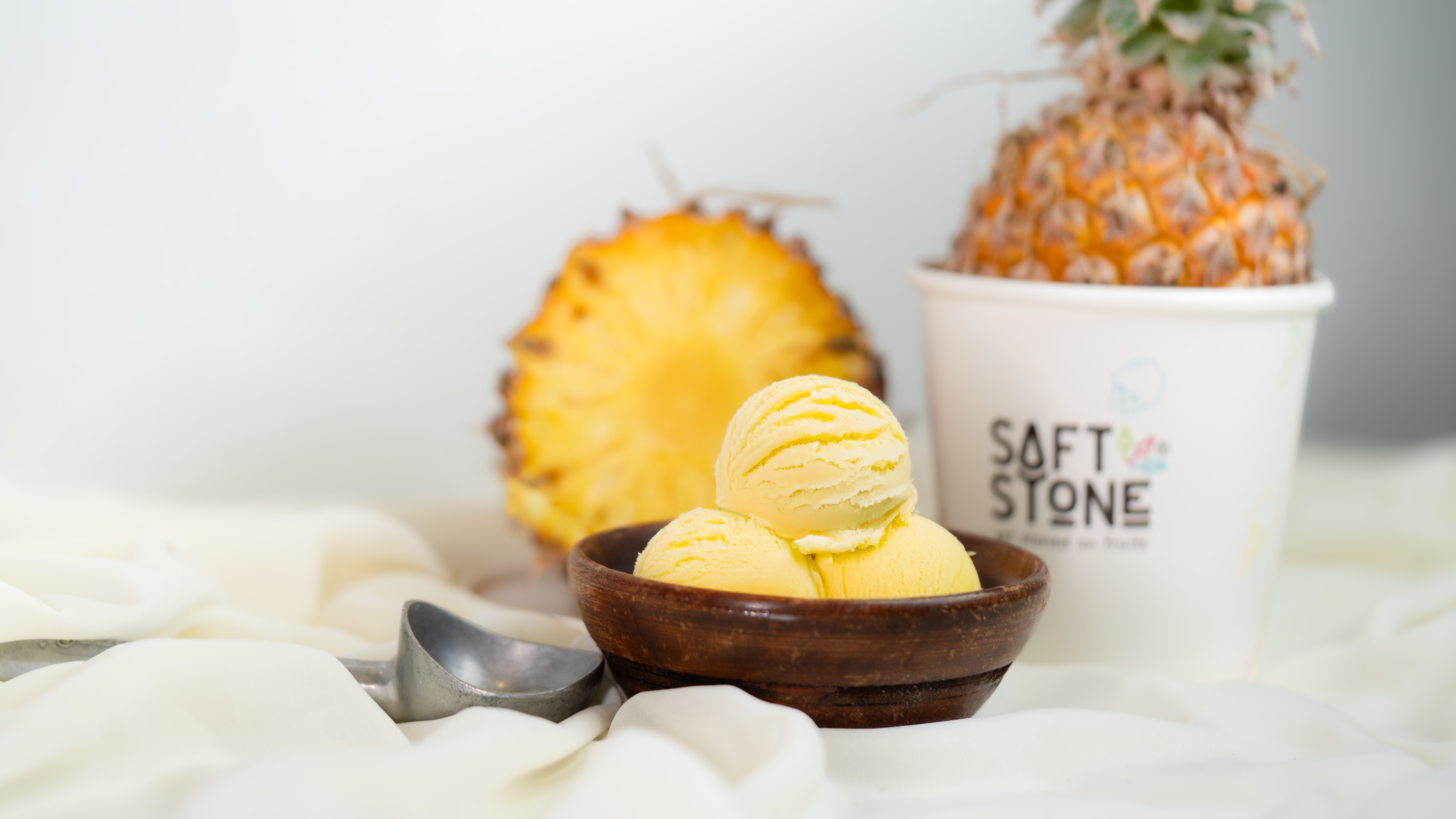 Pineapple ice cream scoops beside a fresh pineapple and Softstone cup